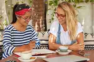 Free photo shot of mixed race women think on common task, write ideas in notepad