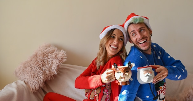 크리스마스 오두막과 재미있는 컵을 들고 옷에 행복한 커플의 샷