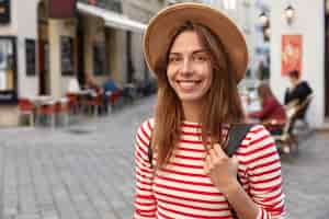 無料写真 素敵な女性の笑顔のショットは、帽子とストライプのジャンパーを身に着けて、街を散歩しながら気分が良いです
