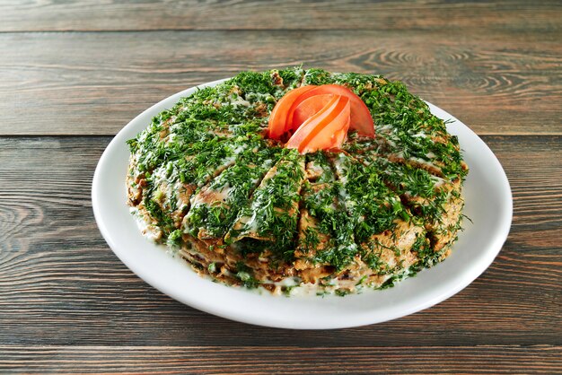 Shot of a pancakes stack sliced and decorated with greens and tomato on top served on the wooden table at the restaurant eating food delicious menu recipe cusine cooking.