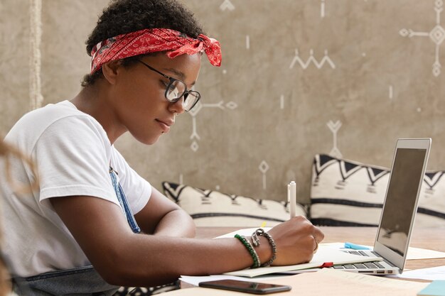 Free photo shot of serious african american student makes notes for making research