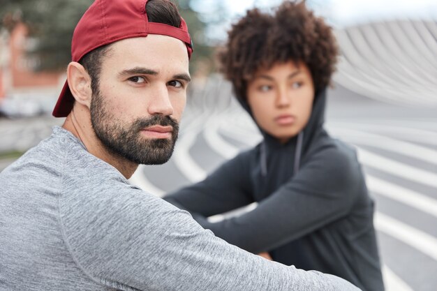 Shot of stylish hipster teenagers spend free time in open air, look thoughtfully somewhere