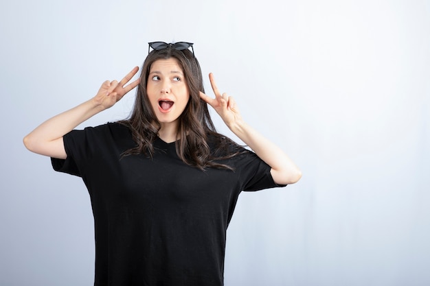 Foto gratuita colpo di giovane donna alla moda in posa in occhiali da sole e mostrando il segno v.