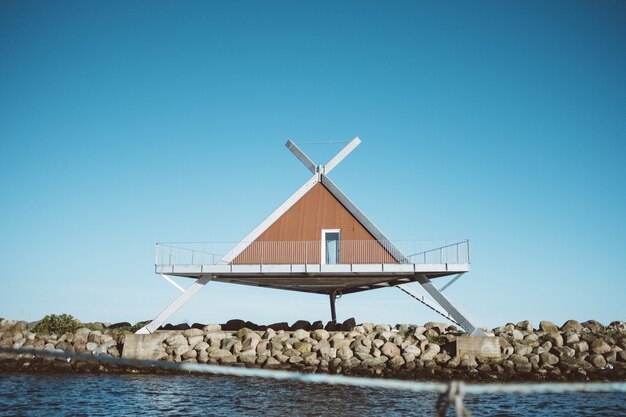 Shot of a triangle-shaped house in front of water under a blue sky