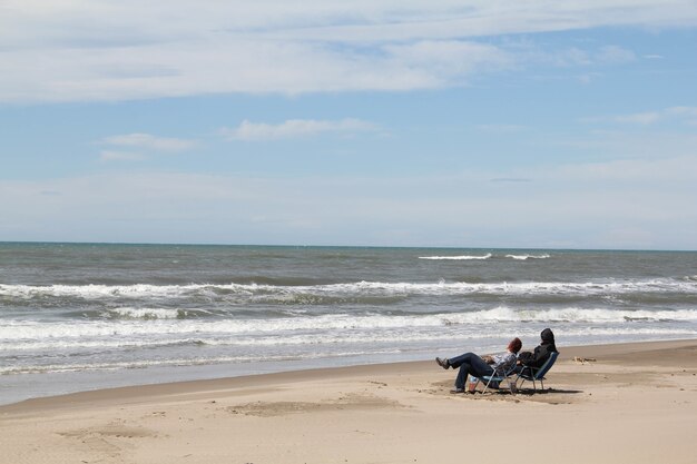 해변의 의자에 앉아 파도를 바라보며 휴식을 취하는 두 사람의 샷