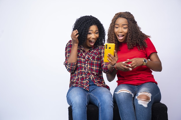 Shot of two young black females looking at the phone together feeling excited and surprised