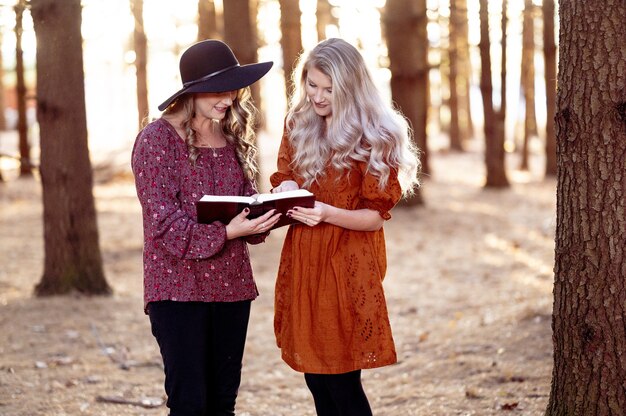 Shot of two young females posing with a book in the forest, autumn mood