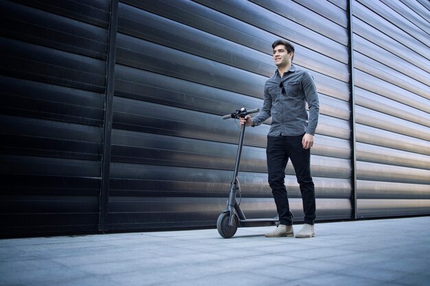 Shot of young handsome man standing by his electric scooter on the street