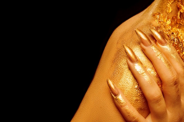 On the shoulder fingers with golden manicure on a black background