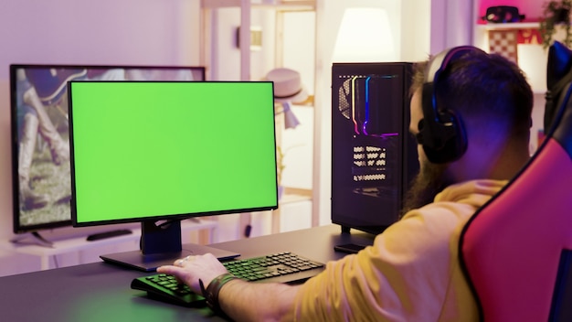 緑色の画面のコンピューターでビデオゲームをプレイしている男性の肩越しの映像。プロのゲームプレイヤー。