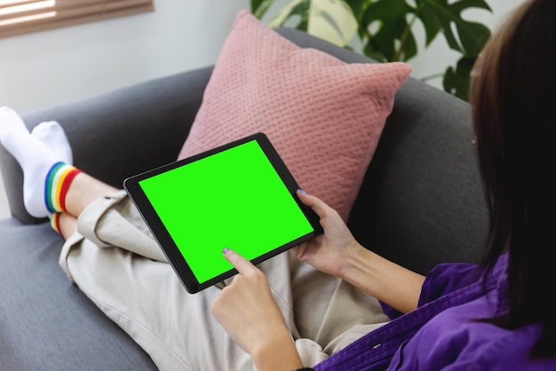 Over shoulder Girl using tablet computer on sofa in living room with blank green screen Work from home concept