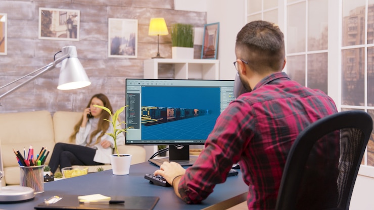 Free Photo over the shoulder shot of young game developer working from home while his girlfriend walks in the backgorund
