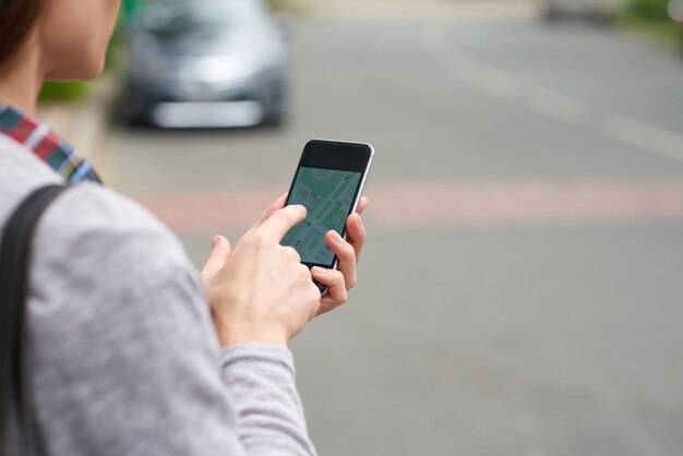 Over the shoulder view of unrecognizable person tracking taxi on the mobile app