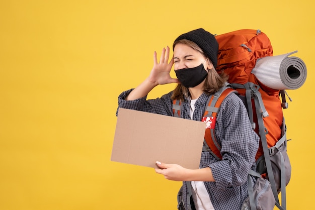 shouting traveler girl with black mask and backpack holding cardboard