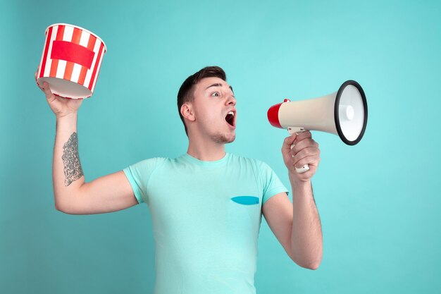 Shouting with popcorn. Caucasian young man's portrait isolated on blue studio wall