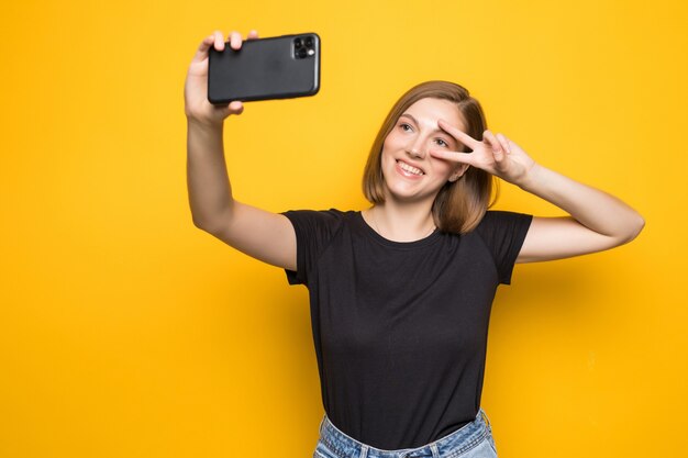 Shouting young woman taking a selfie photo on yellow wall.