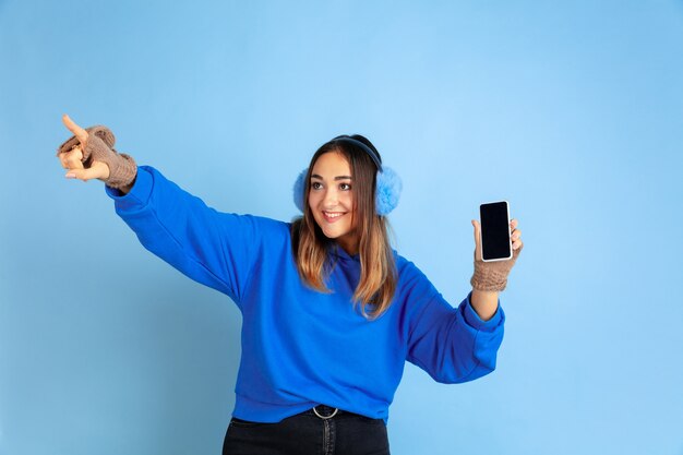 Showing blank screen. Caucasian woman's portrait on blue  space. Beautiful female model in warm clothes