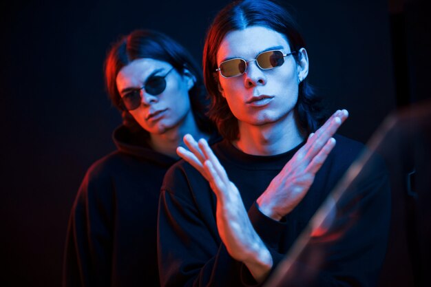 Showing gesture that means stop or don't. Portrait of twin brothers. Studio shot in dark studio with neon light