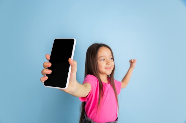 Showing phone's screen. Caucasian little girl's portrait on blue wall.