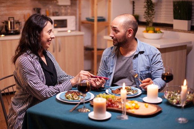 ロマンチックな夕食の間に夫に陽性の妊娠検査を示しています。この素晴らしいニュースのためにお互いに微笑んで、抱き合って、キスして興奮したカップル。妊娠中の若い妻は、男性を受け入れる結果に満足しています。