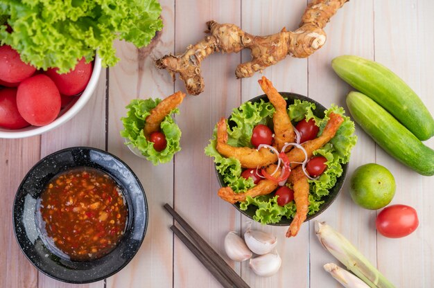 Shrimp deep fried batter placed on salad and tomatoes in a wooden bowl.