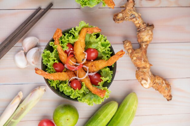 Shrimp deep fried batter placed on salad and tomatoes in a wooden bowl.