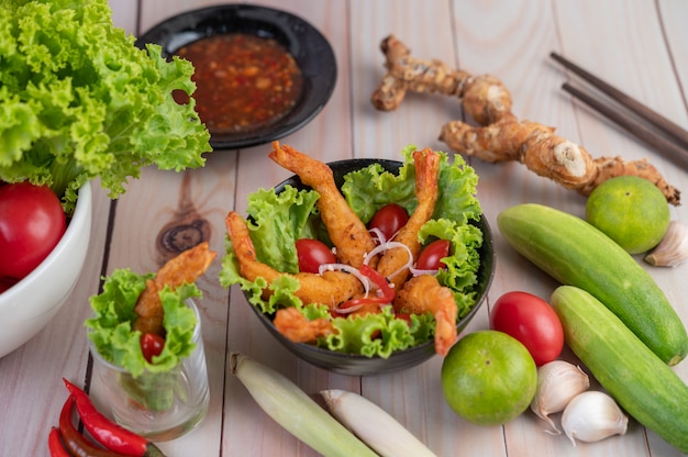 Shrimp deep fried batter placed on salad and tomatoes in a wooden bowl.