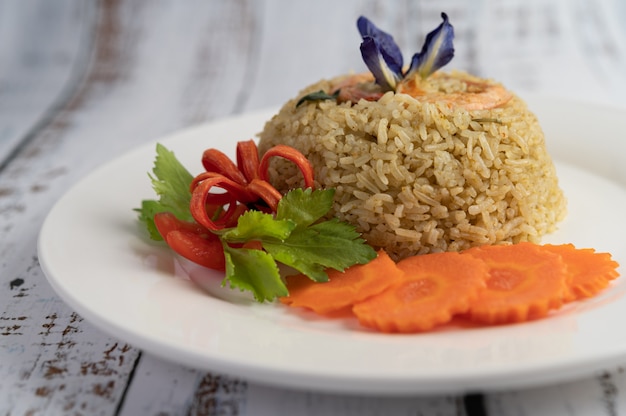 Жареный рис с креветками на белой тарелке, состоящей из помидоров и моркови.