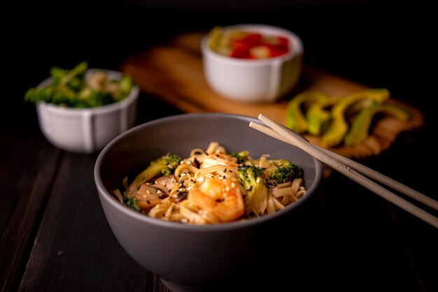 Shrimp on noodles in bowl with avocado and chopsticks