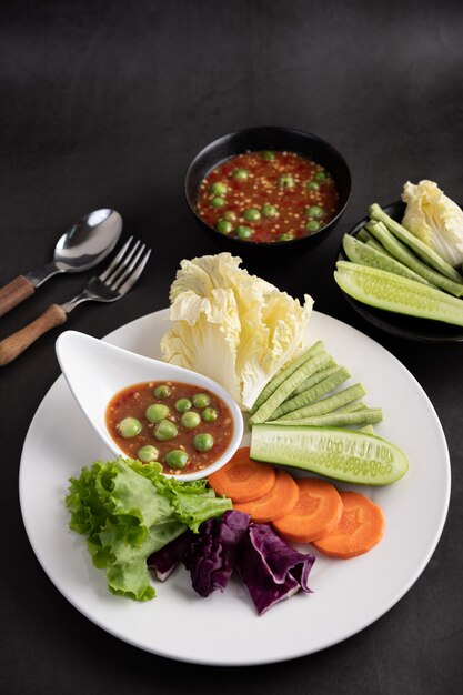 Креветочно-пастообразный соус в миске на белой тарелке с огурцом, двориком, тайским баклажаном, жареной белокочанной капустой, морковью и салатом