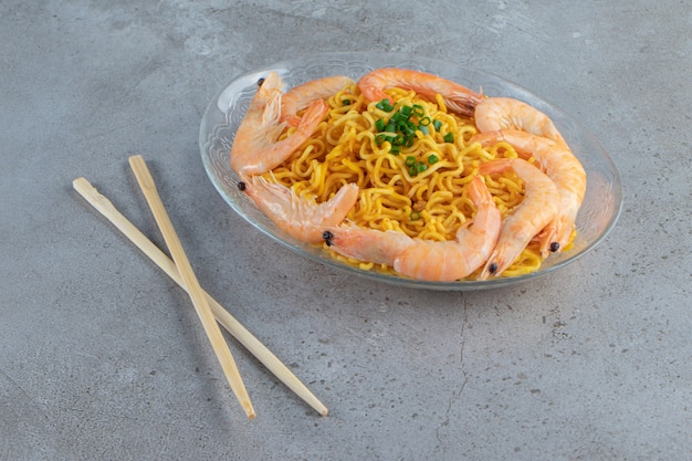 Shrimps and noodle on a glass dish next to chopsticks, on the marble background. 