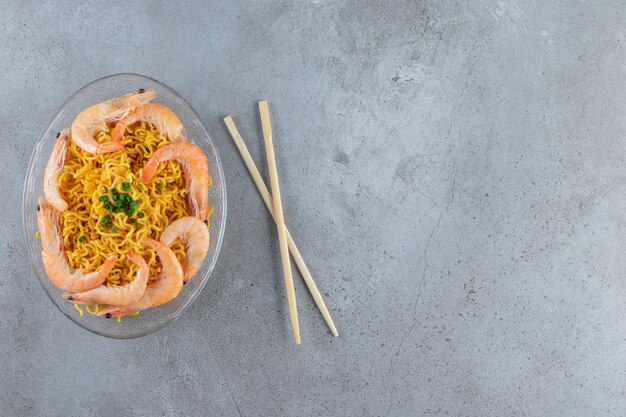 Shrimps and noodle on a glass dish next to chopsticks, on the marble background. 