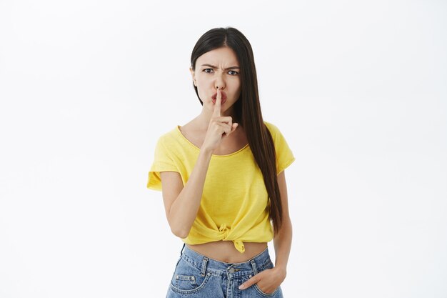 Shut up. Angry irritated beautiful woman in yellow t-shirt shushing with annoyed face frowning wrinkling nose in anger