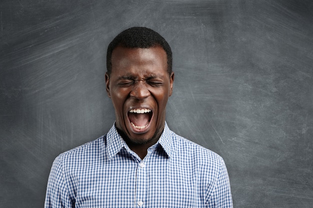 Shut up! Headshot of annoyed furious African high-school teacher yelling at his disobedient students, calling for silence, with closed eyes and mouth wide open.