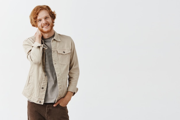 Shy bearded redhead guy posing against the white wall
