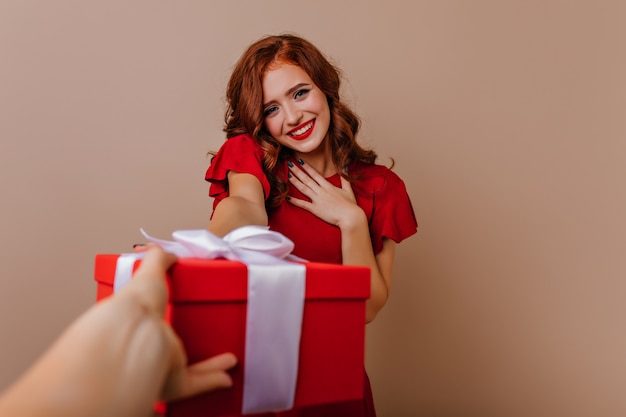 彼女の誕生日にポーズをとって赤いドレスを着た恥ずかしがり屋の美しい少女。新年のプレゼントと巻き毛に触発された女性の屋内写真。