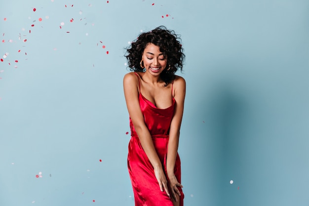 Shy curly woman standing under confetti