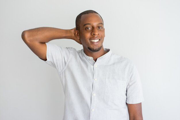 Shy handsome African-American guy scratching back of head and looking at camera.