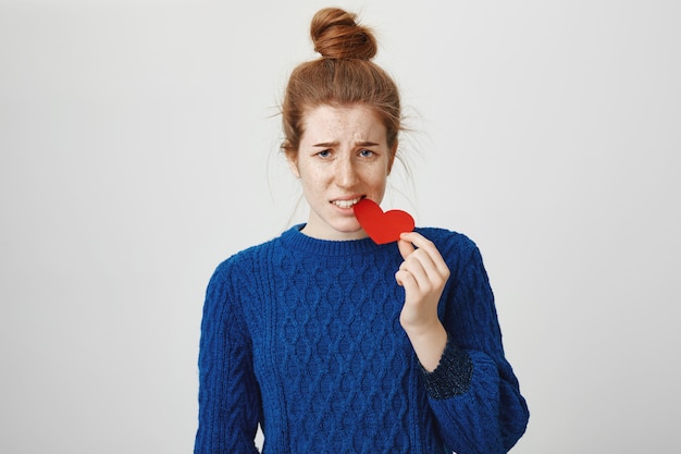 Shy redhead girl biting heart sign and looking frustrated