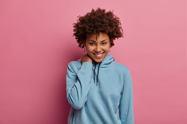 Shy romantic curly woman smiles happily, touches neck