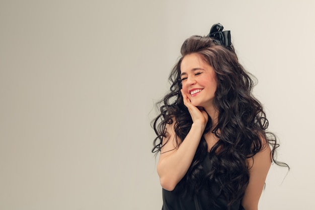 Shy smiling. Portrait of beautiful young woman on grey studio