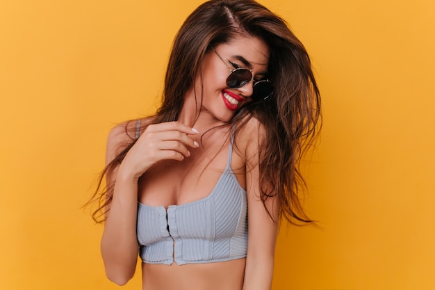 Shy tanned woman in tank-top looking down with smile