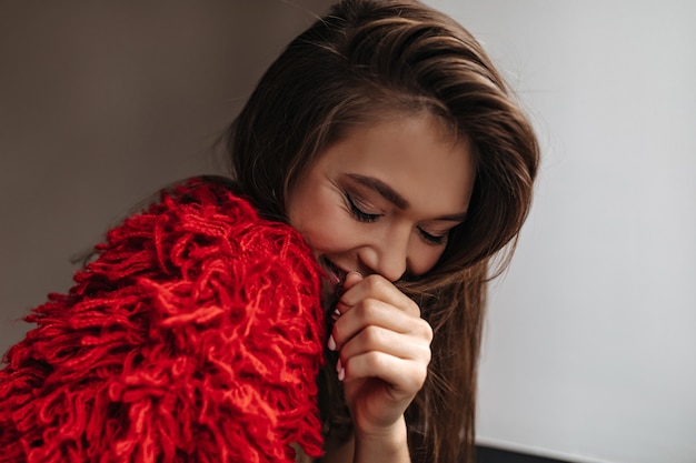 Shy woman in bright red woolen outfit smiling, covering her mouth on white background.