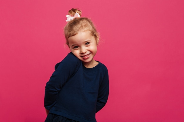 恥ずかしがり屋の若いブロンドの女の子のポーズとピンクの壁の上のカメラを見て