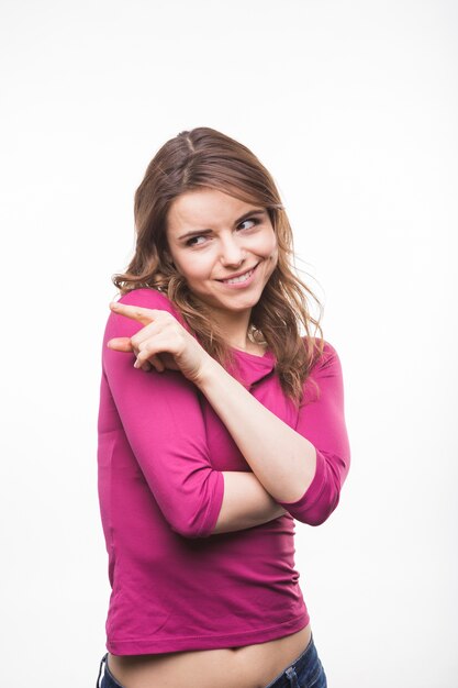 Shy young woman pointing at something standing against white background