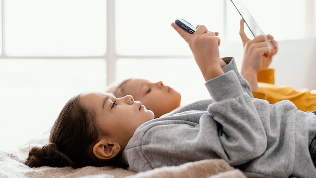 Siblings in bed playing on mobile and tablet