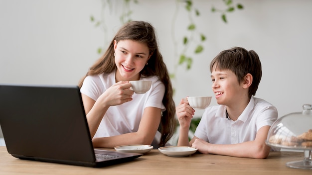 Siblings drinking tea and using laptop