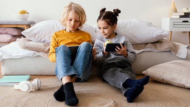 Siblings playing with mobile and tablet