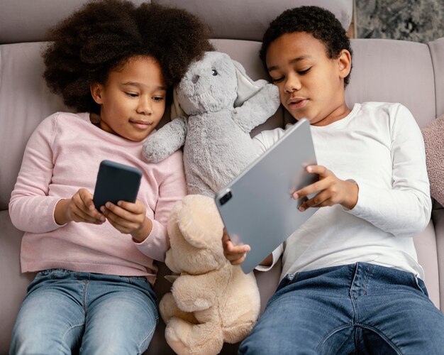 Siblings using tablet and mobile at home