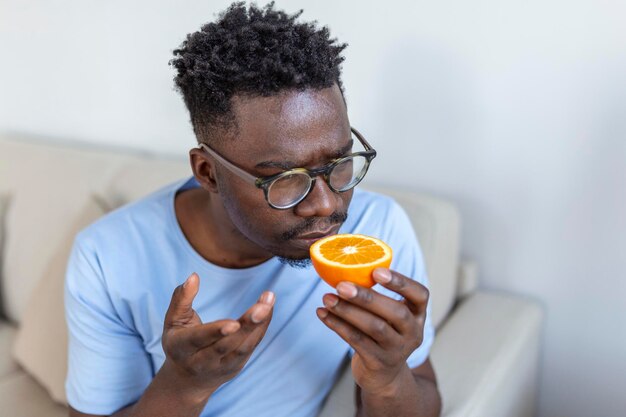 Sick Arican man trying to sense smell of half fresh orange has symptoms of Covid19 corona virus infection loss of smell and taste One of the main signs of the disease